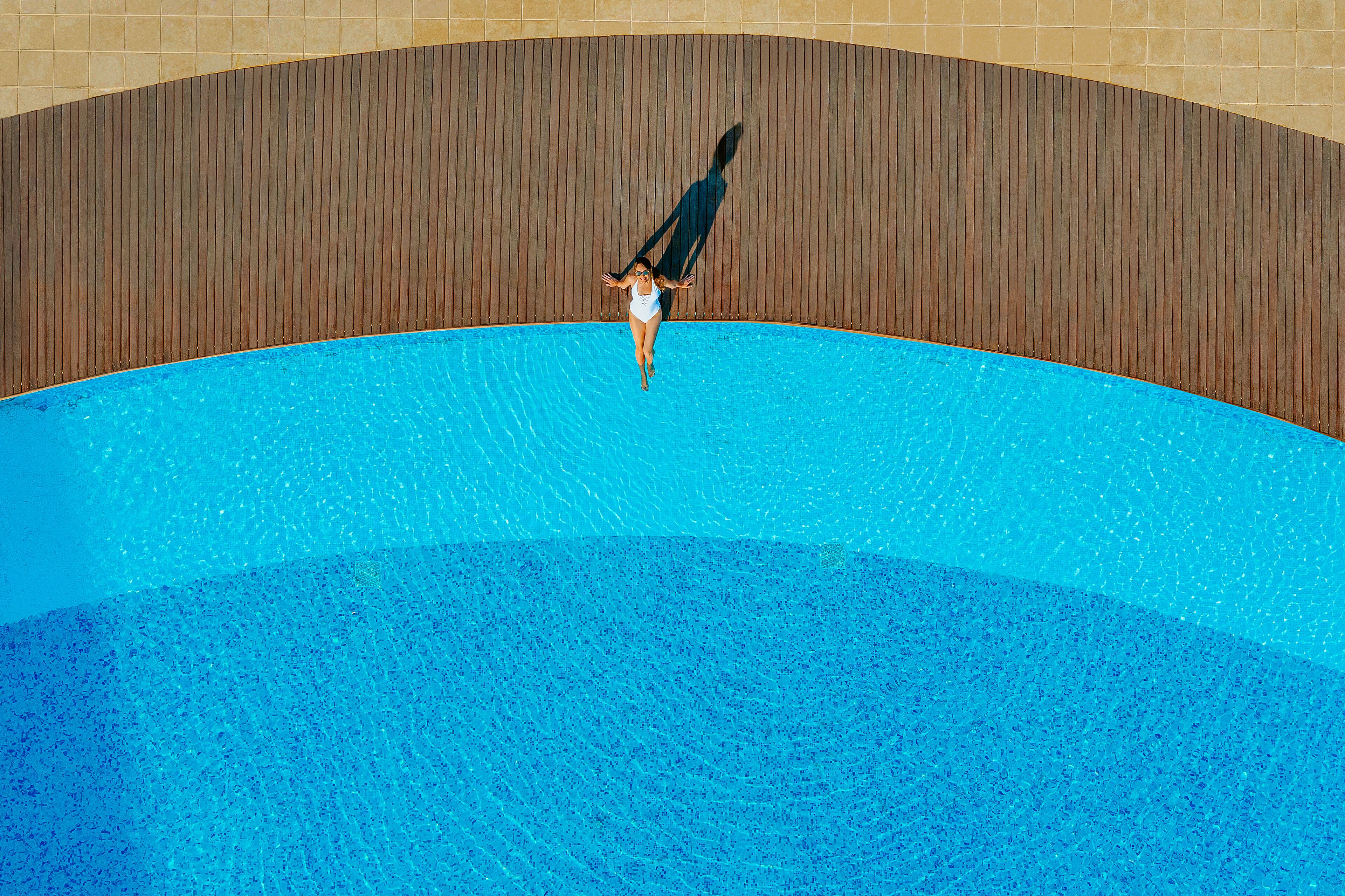A person in a white swimsuit standing in a swimming pool with a wooden wall in the background.