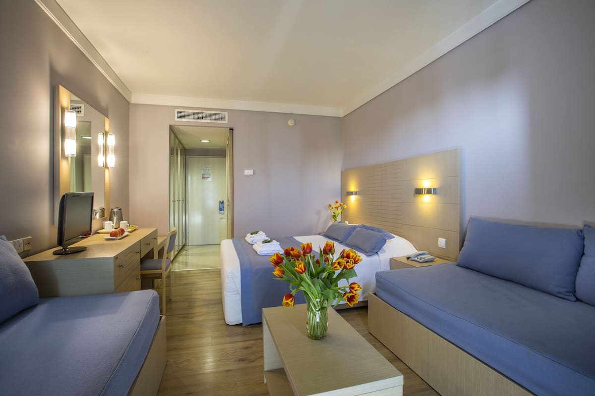 A modern hotel room with a bed, a sofa, a desk, and a vase of flowers.
