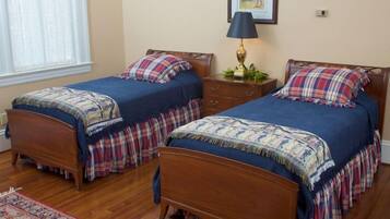 A bedroom with two wooden beds, a nightstand with a lamp, a framed picture on the wall, and a window with sheer curtains.
