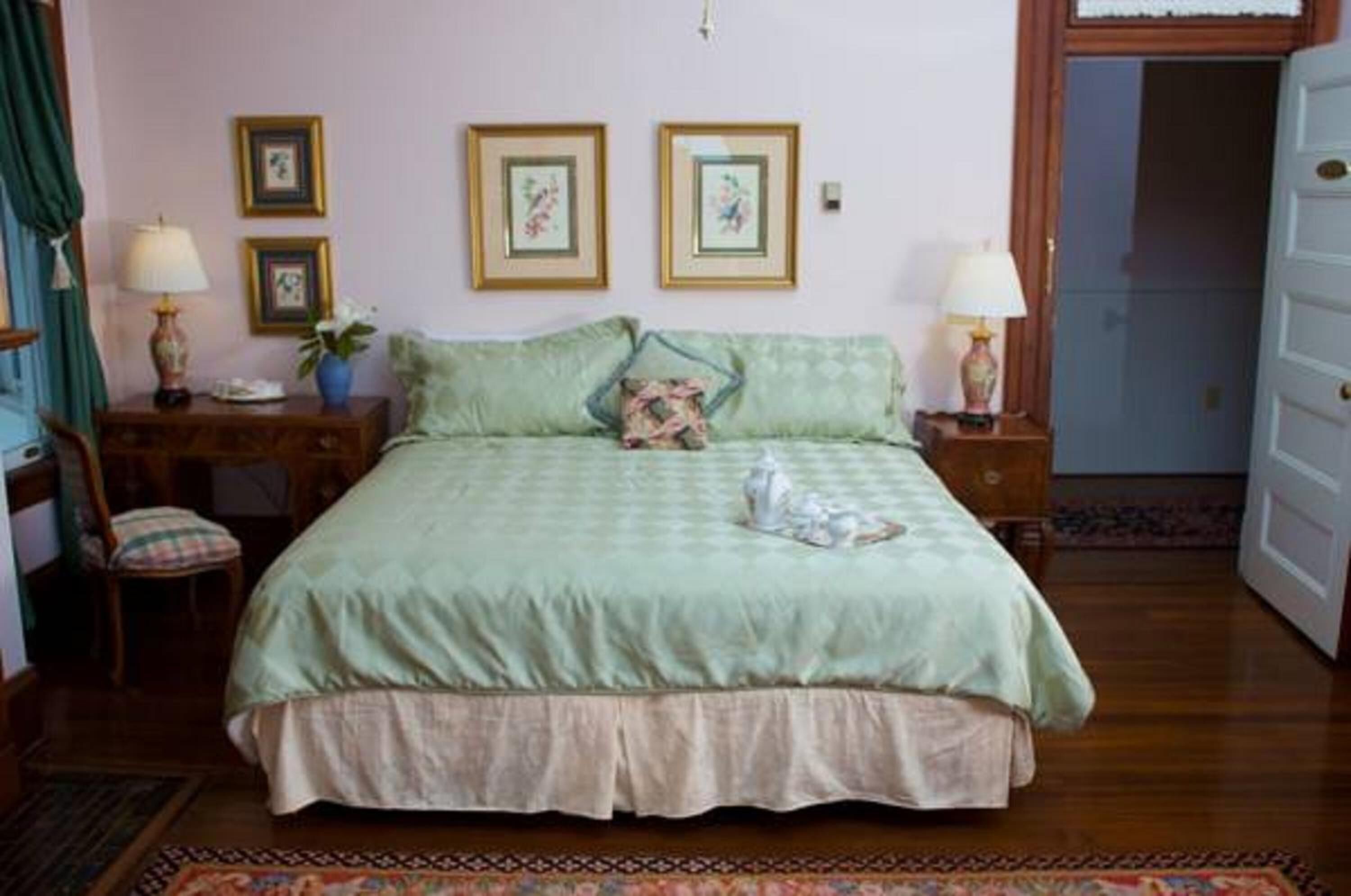 A bedroom with a bed, two bedside tables with lamps, a chair, and a door.