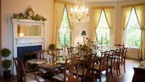 A formal dining room with a fireplace, chandelier, and large windows with curtains. - Lookaway Inn (North Augusta)