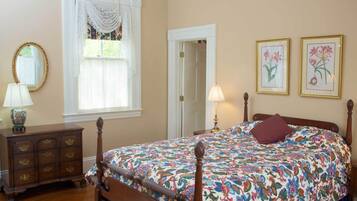 A bedroom with a floral bedspread, a wooden dresser, a mirror, and two framed floral paintings on the wall.