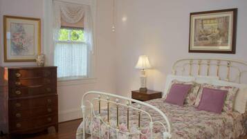 A bedroom with a bed, dresser, window, and paintings.