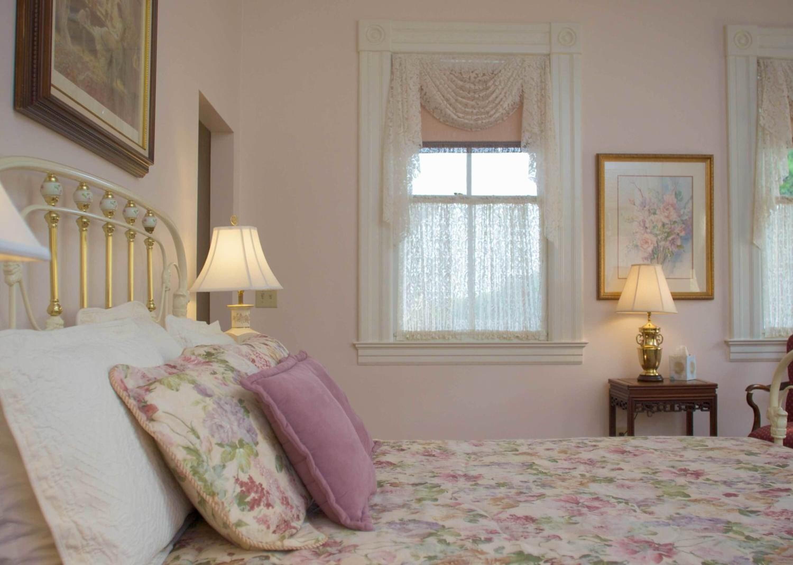 Une chambre à coucher avec un lit, deux tables de chevet, une fenêtre avec des rideaux et un tableau au mur.