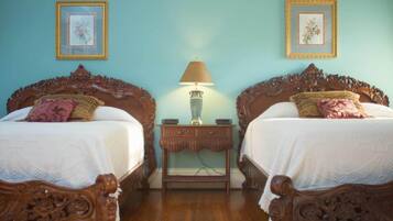 A room with two ornate wooden beds, a small nightstand with a lamp, and floral wall art.