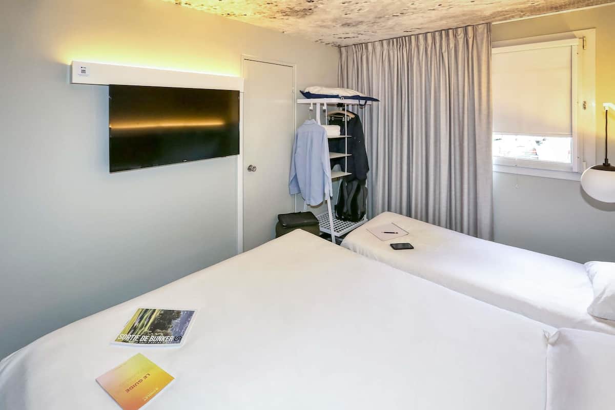 A hotel room with two beds, a wardrobe, a TV, and a window with curtains.