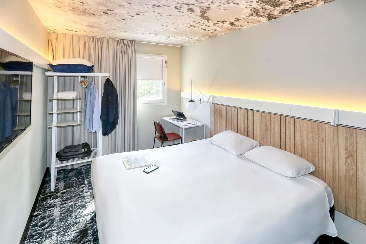 A hotel room with a bed, a desk, a chair, a wardrobe, and a window.