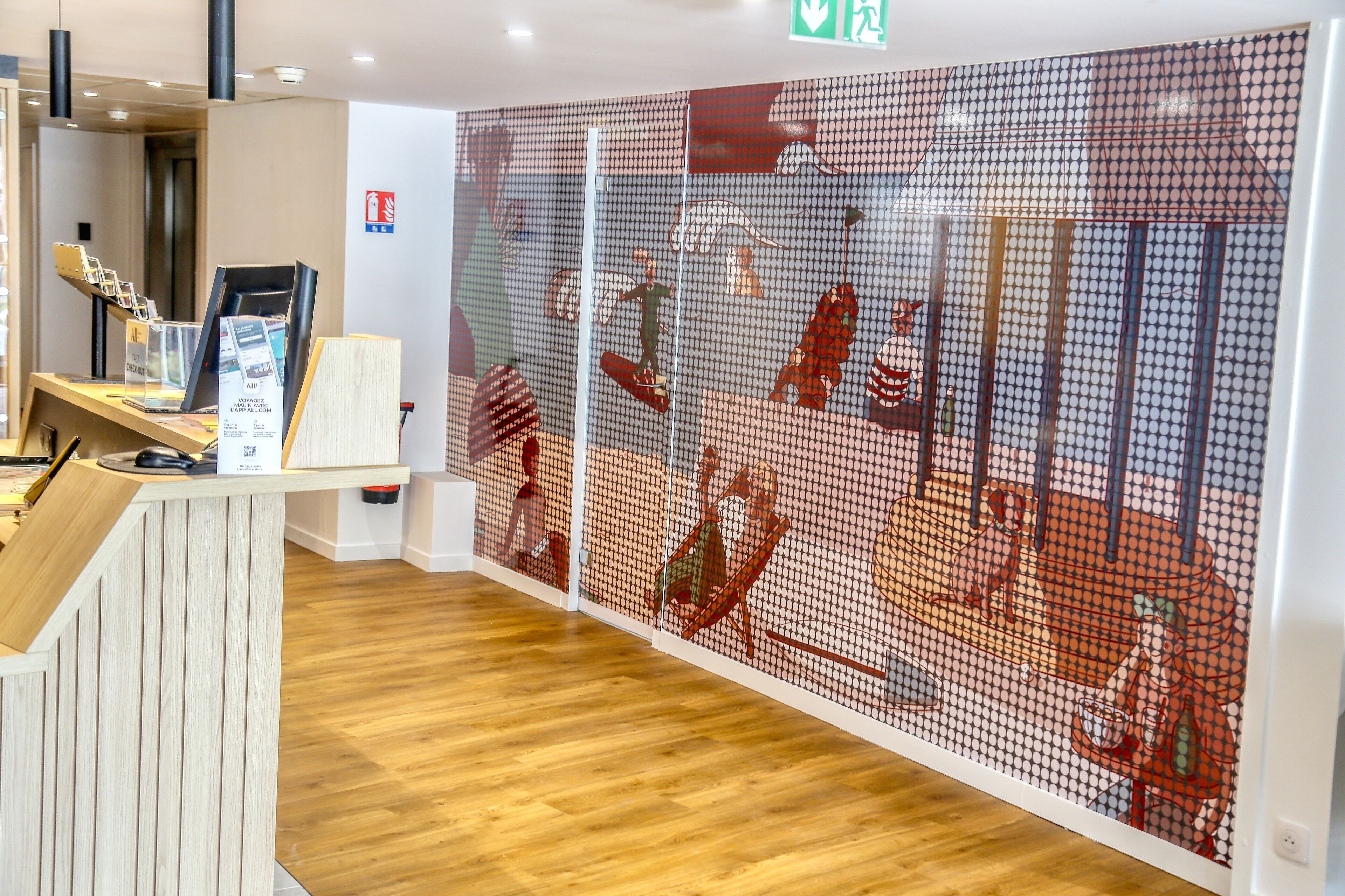 A reception area with a wooden desk, a digital screen, and a wall with a red and white mural.