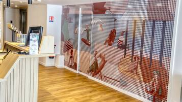 A reception area with a wooden desk, a digital screen, and a wall with a red and white mural.