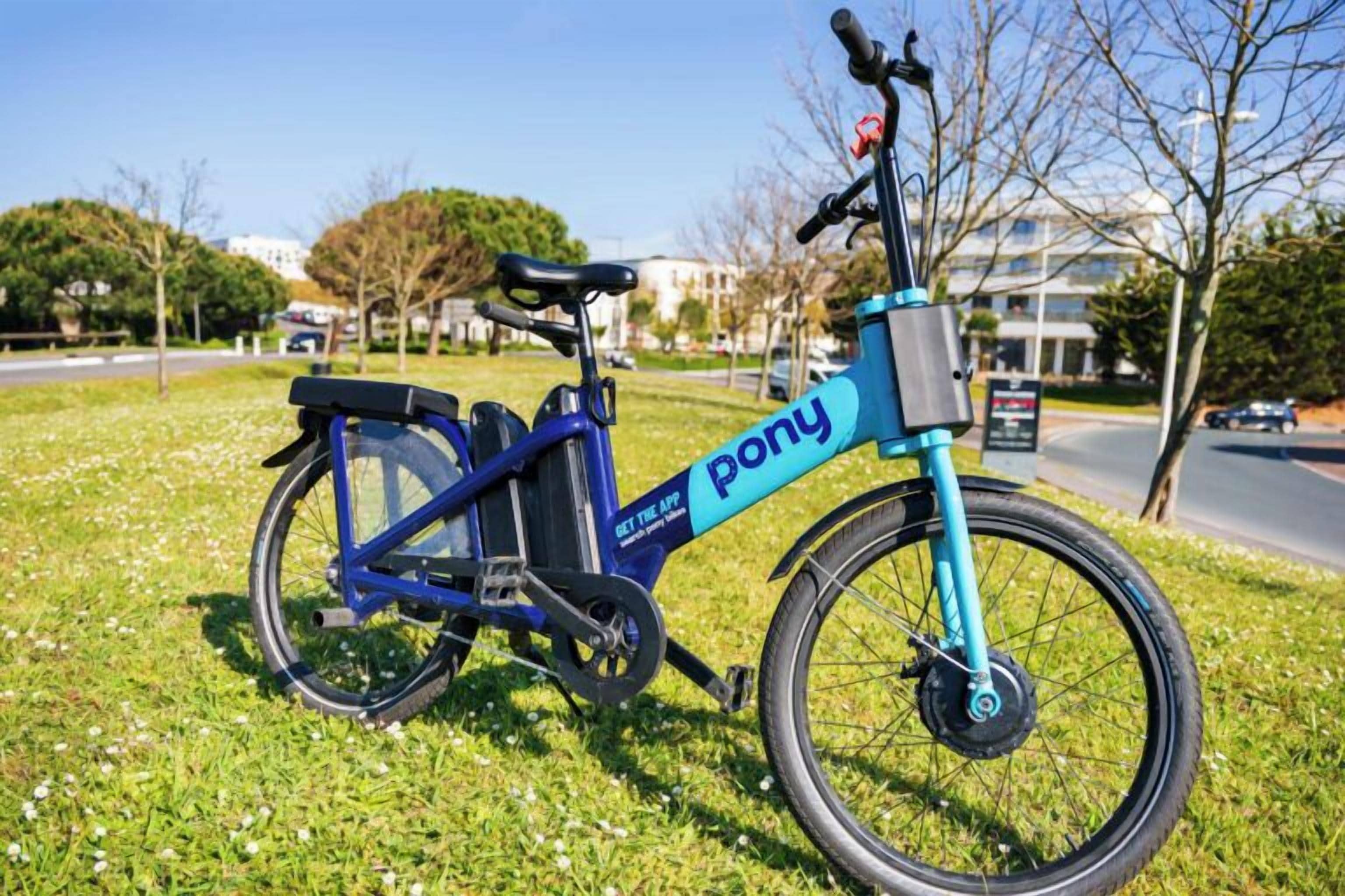 A stationary blue electric bike with 'pony' branding on a grassy area.