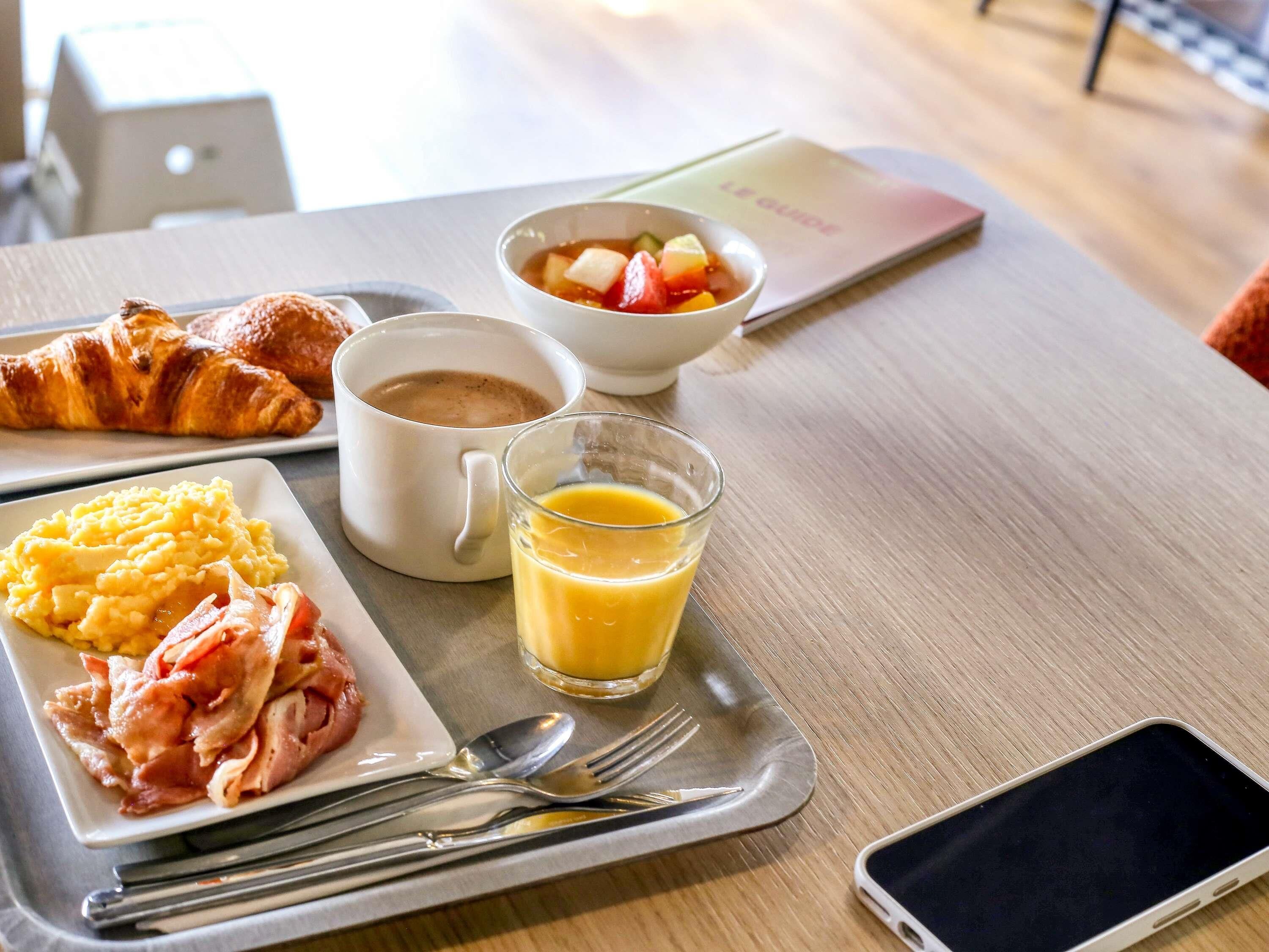 A breakfast tray with croissants, scrambled eggs, ham, a mug of coffee, a glass of orange juice, and a bowl of fruit salad.