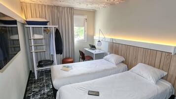 A hotel room with two beds, a desk with a laptop, a chair, a wardrobe, and a window.