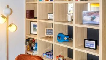 Una habitación con una estantería de madera, un cuadro enmarcado, una guitarra azul y un tablero de ajedrez.