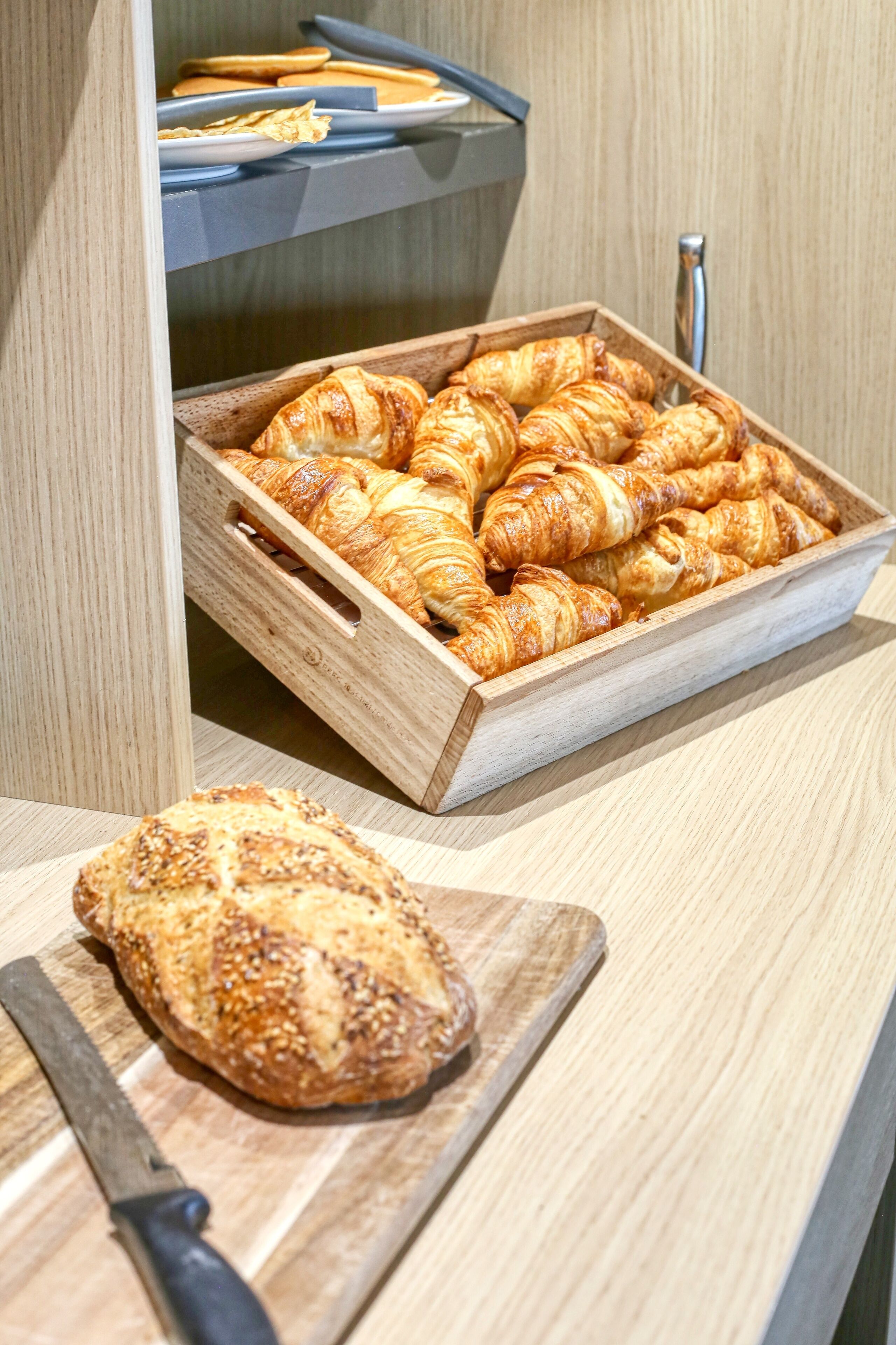 A wooden counter with a tray of croissants and a loaf of bread on a cutting board.