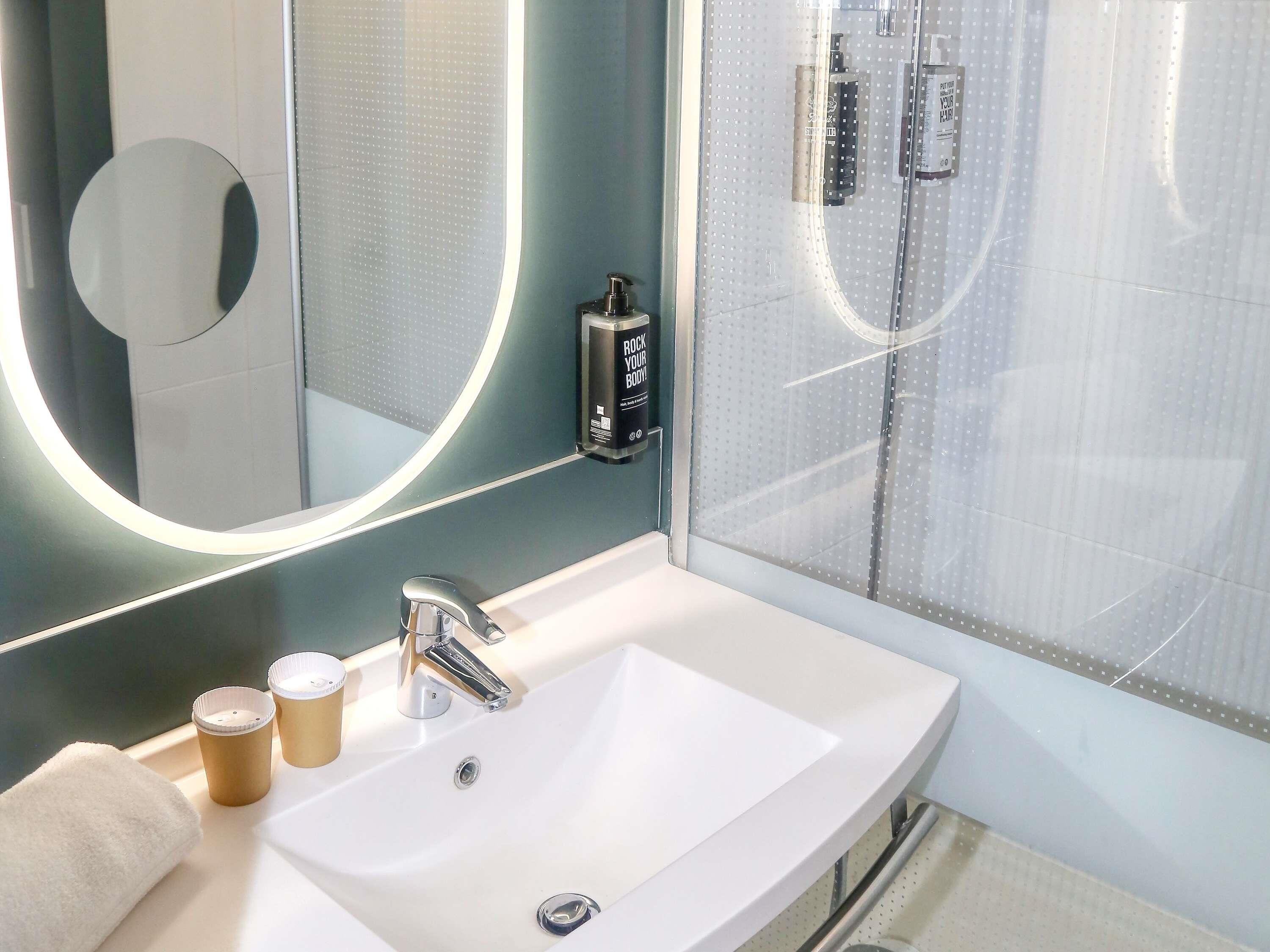 A modern bathroom with a white sink, a round mirror, and a glass shower enclosure.
