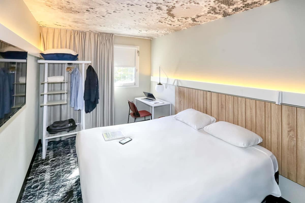 Une chambre d’hôtel comprenant un lit, un bureau, une chaise, une armoire et une fenêtre.