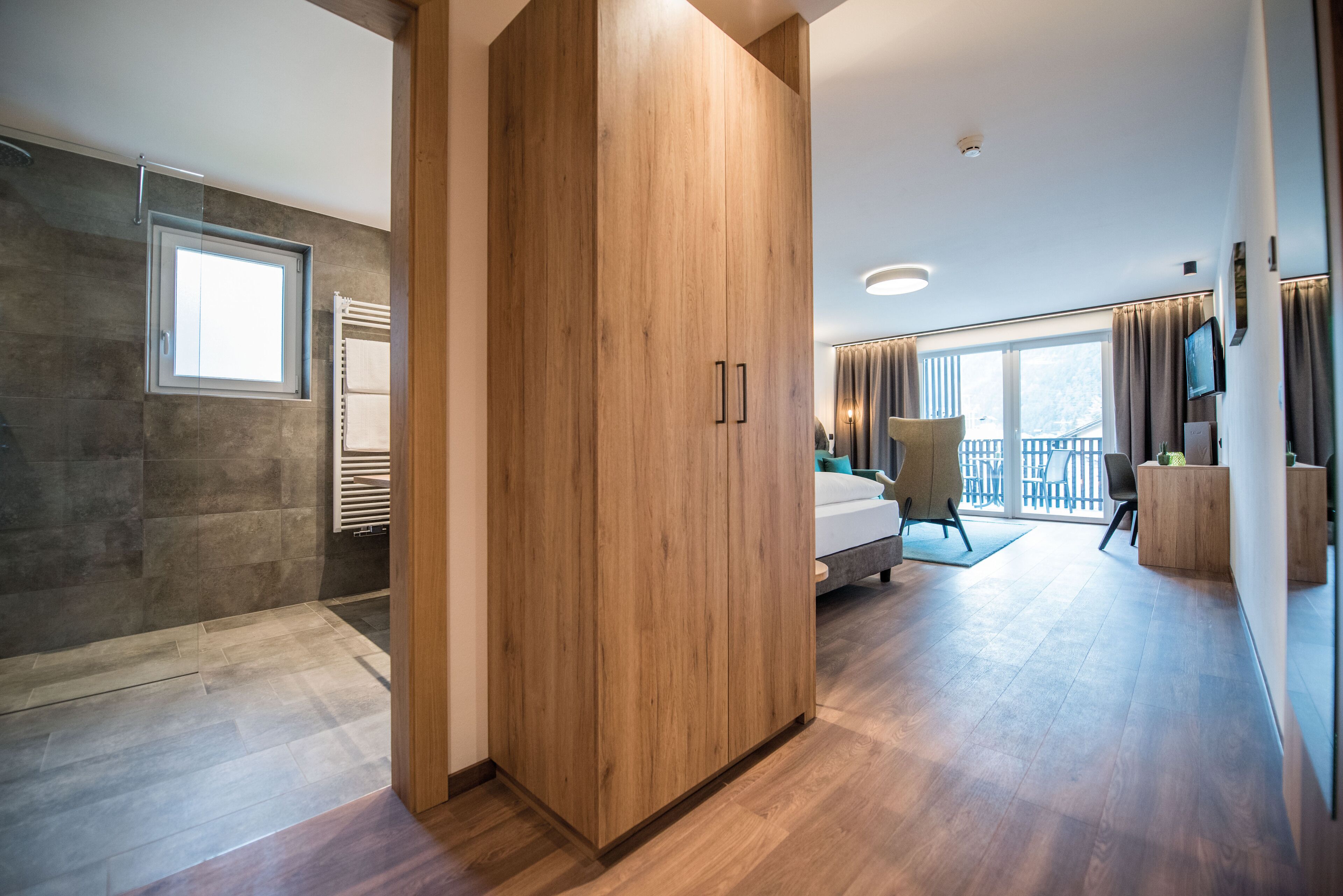 Ein modernes Hotelzimmer mit großem Kleiderschrank, einem Bett, einer Sitzecke und einem Balkon mit Blick.