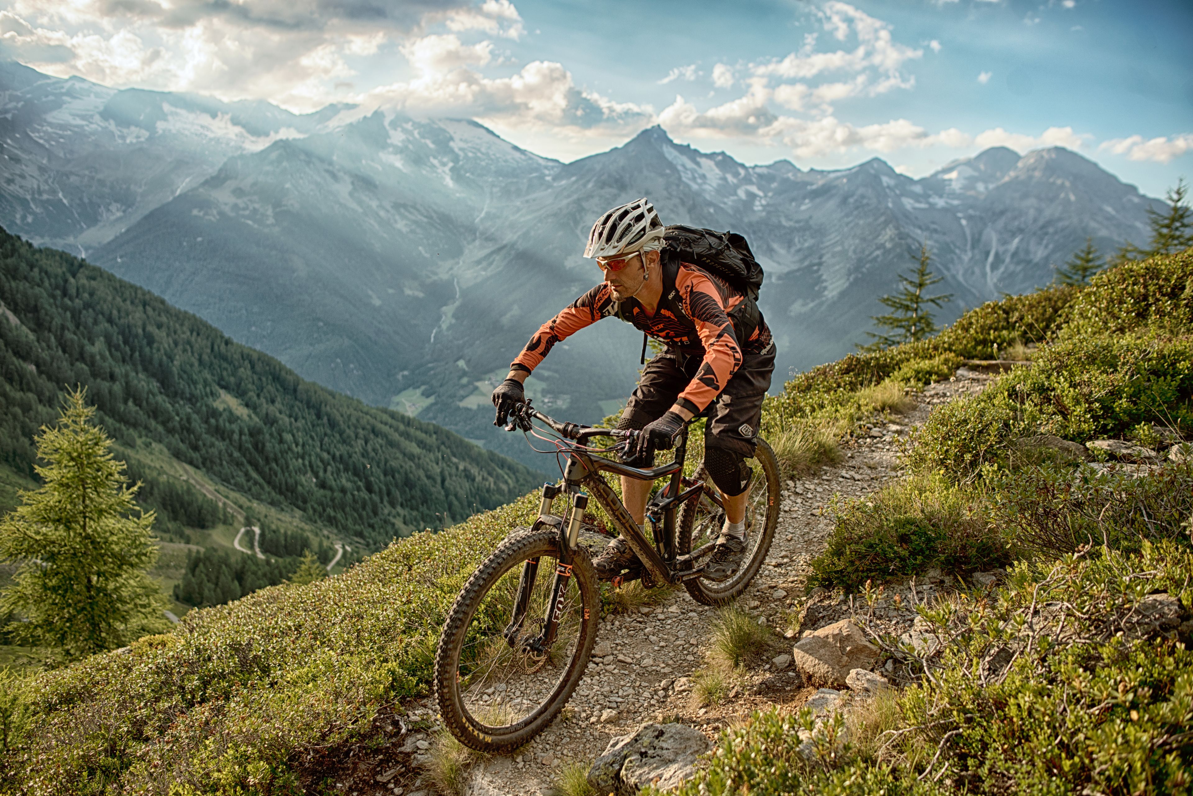 A mountain biker on a trail with a mountainous backdrop.