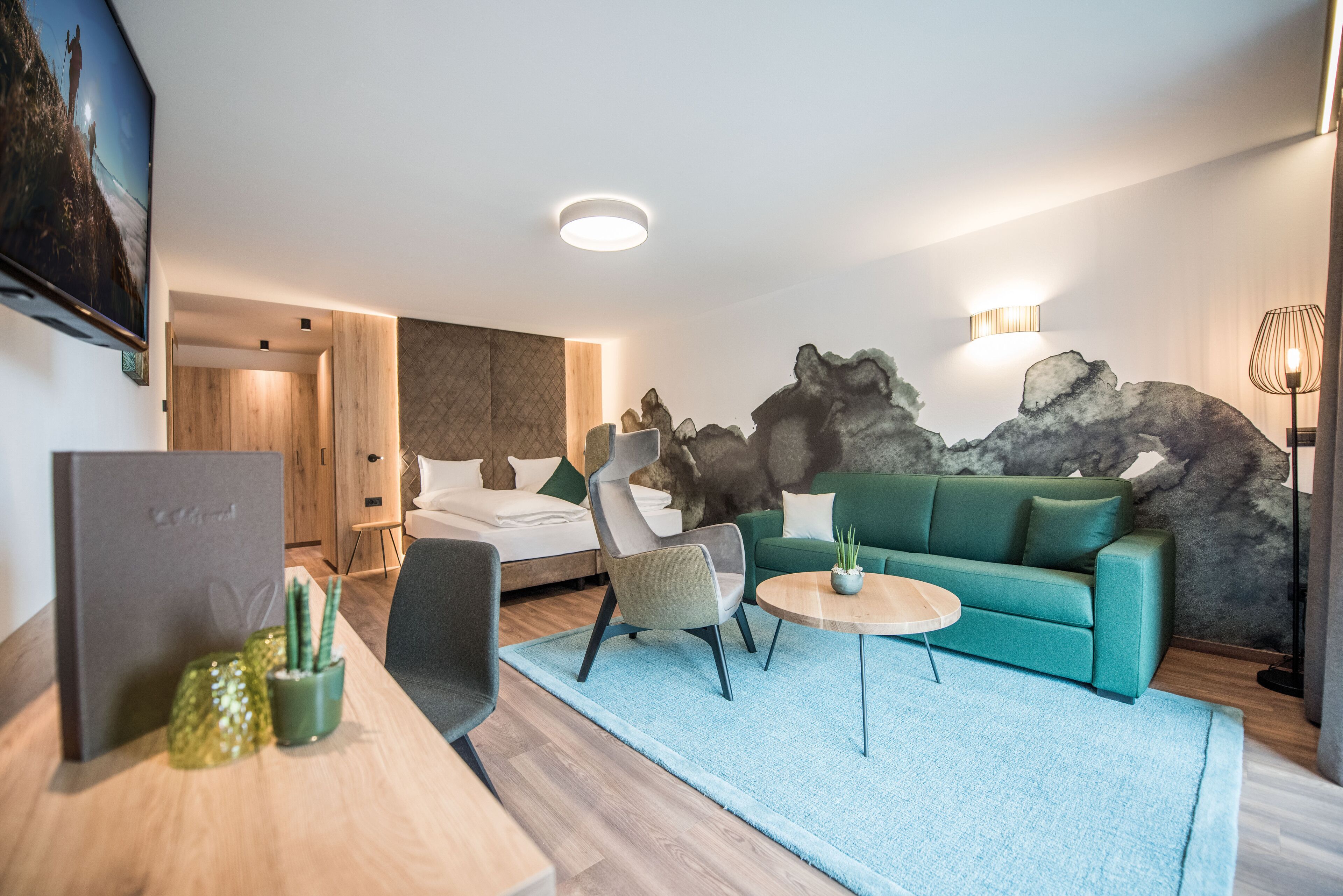 A modern hotel room with a bed, a green sofa, a small table, and a TV.