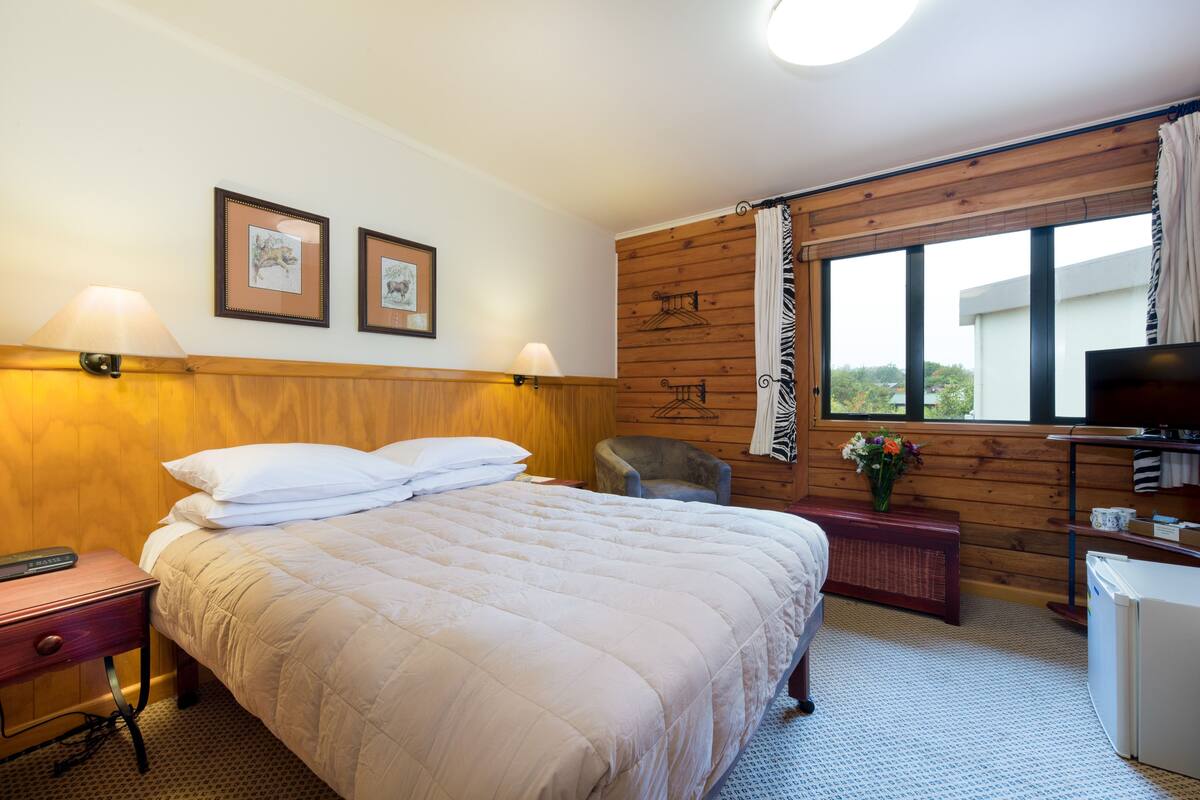 Une chambre d’hôtel avec un grand lit, une chaise, un bureau avec un ordinateur, une télévision et des tableaux encadrés au mur.