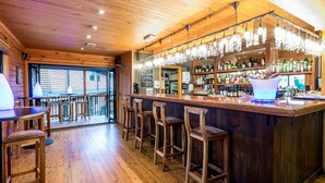 A wooden bar area with a long counter, bar stools, and a variety of bottles and glasses.