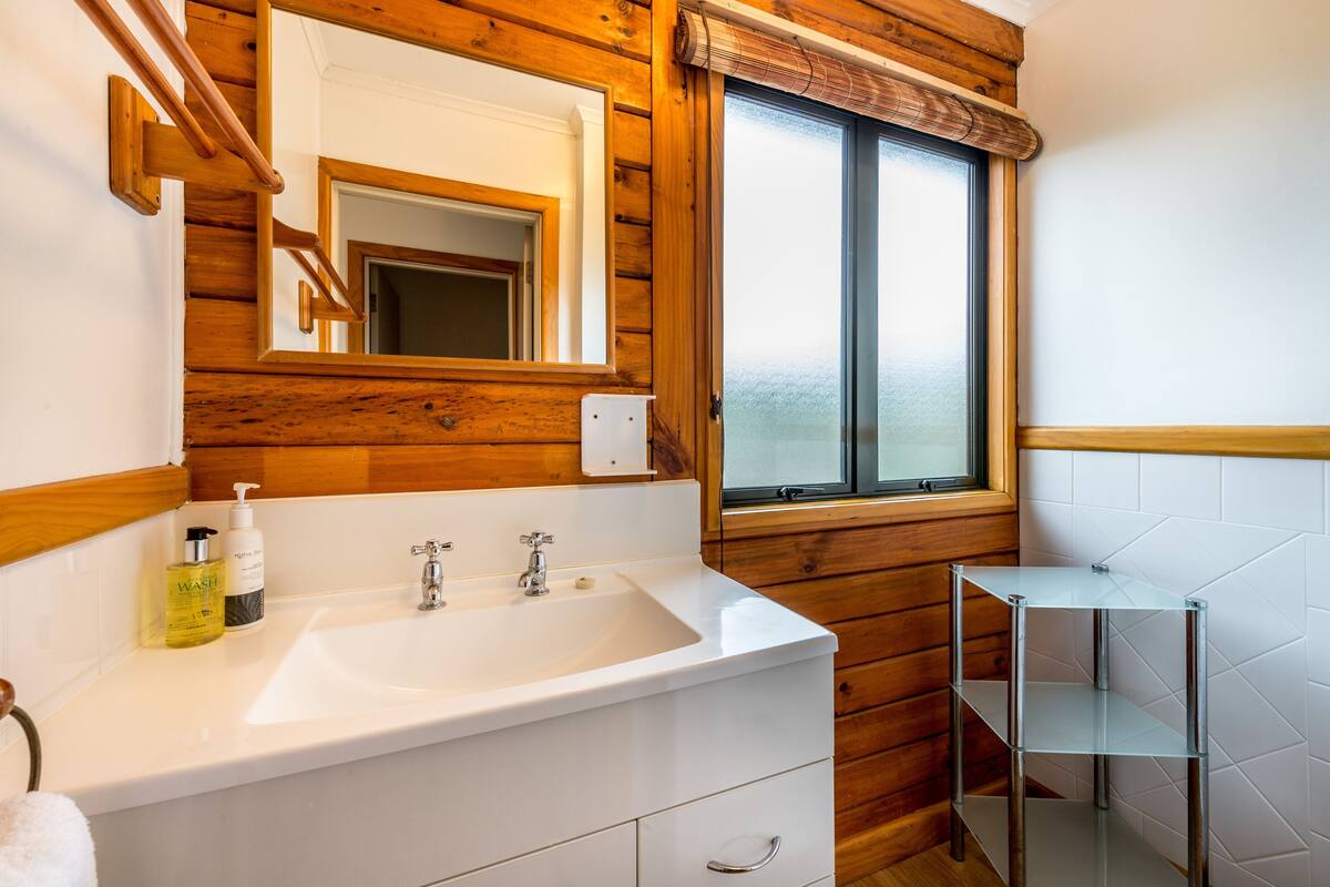 Une salle de bain avec un intérieur en bois, un lavabo blanc doté de deux robinets, un miroir et une fenêtre.