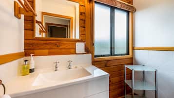 A bathroom with a wooden interior, a white sink with two faucets, a mirror, and a window.