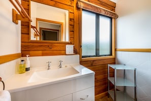 A bathroom with a wooden interior, a white sink with two faucets, a mirror, and a window.