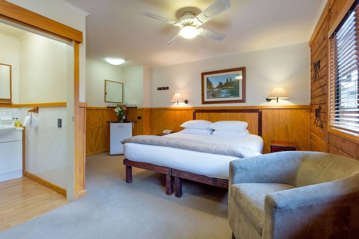 Une chambre à coucher comprenant un lit, des tables de chevet, une chaise, un ventilateur de plafond et une fenêtre avec des stores.