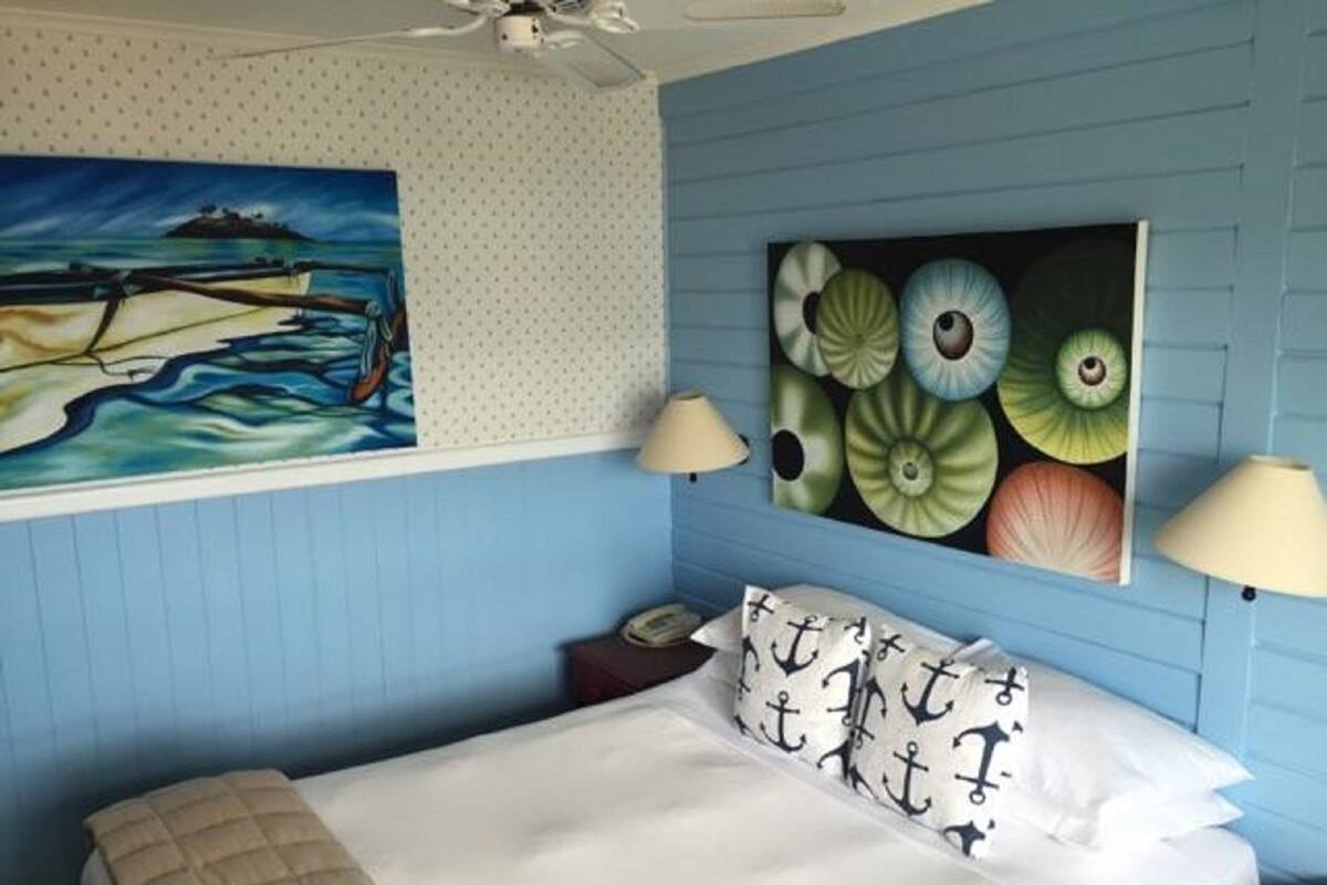 Une chambre à coucher comprenant un lit, deux tables de chevet, un ventilateur de plafond et des œuvres d’art murales.