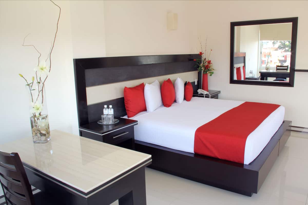 A modern hotel room with a large bed, a bedside table, a nightstand, a mirror, and a vase with flowers.