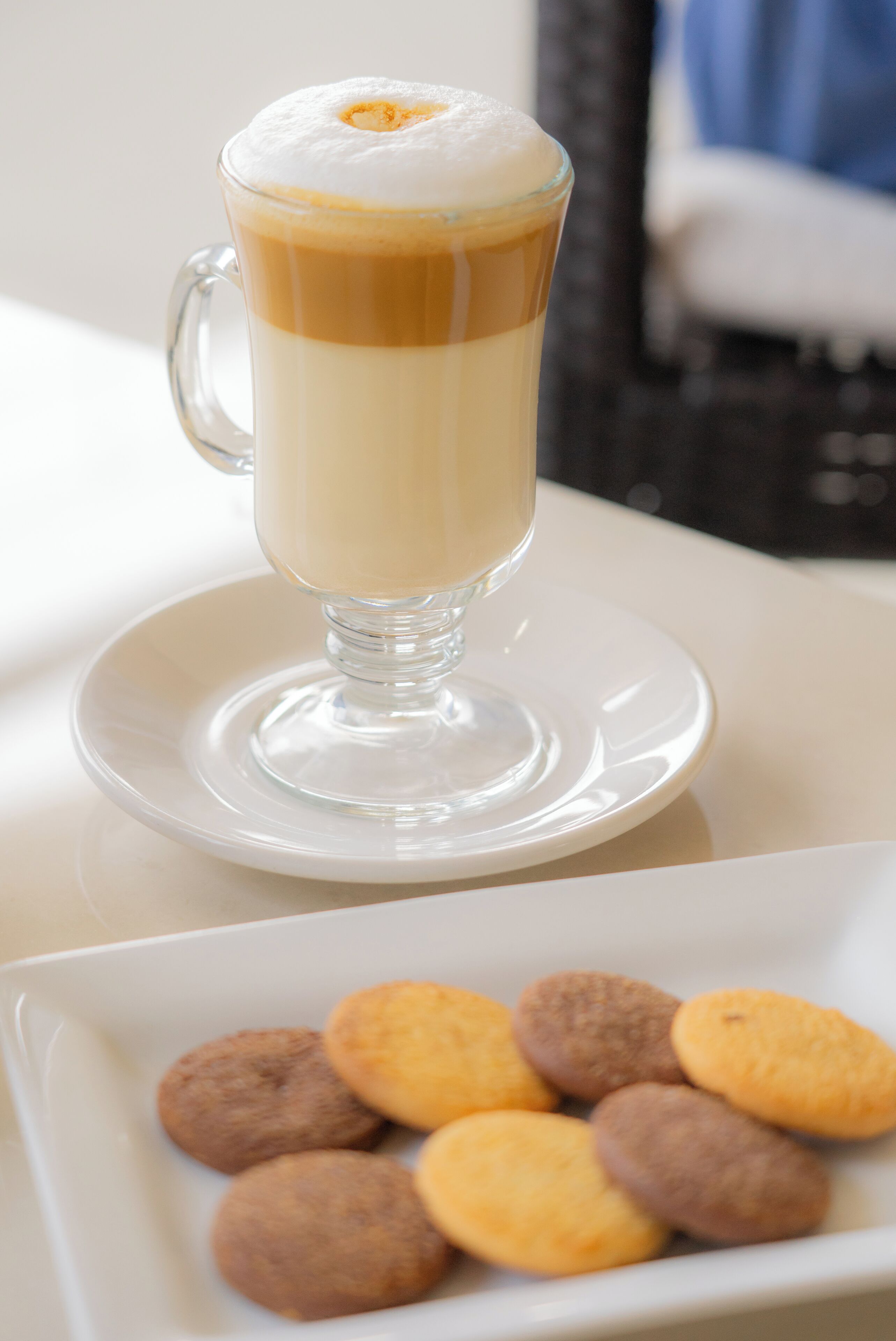 Una taza de café de vidrio transparente con un diseño en capas, sobre un plato blanco.