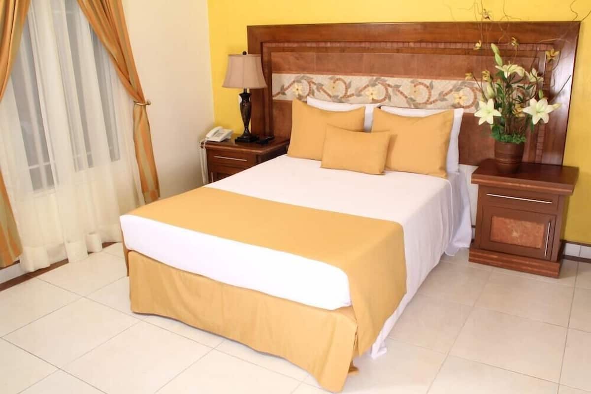 A hotel room with a large bed, a wooden headboard, a nightstand with a lamp, and a vase with flowers.