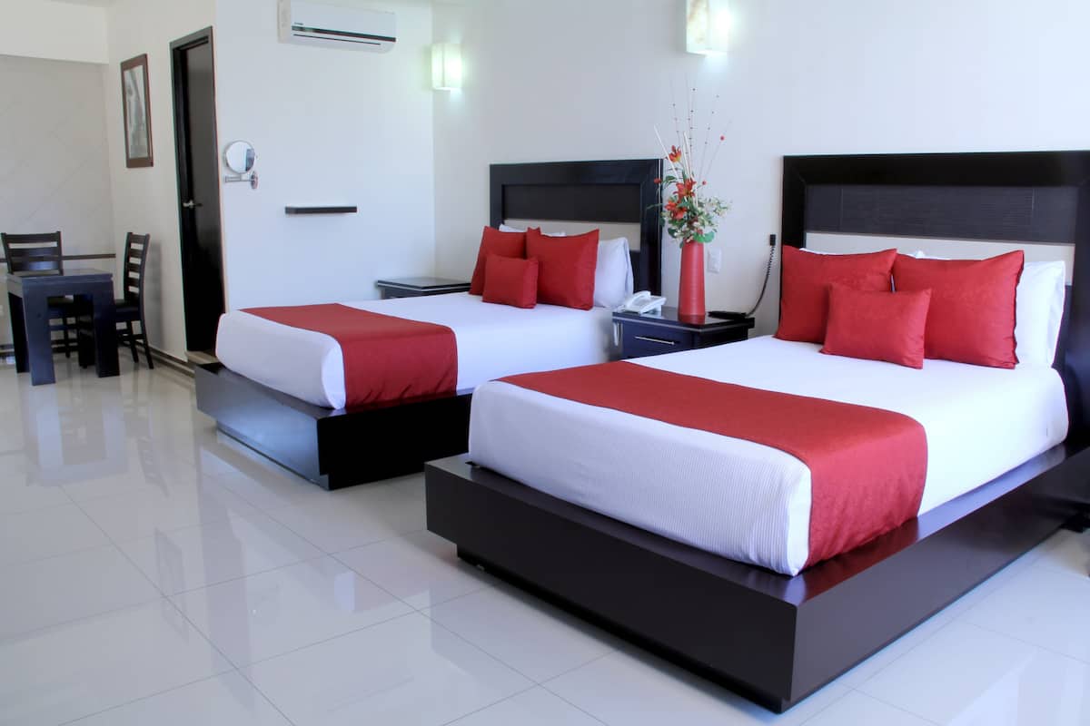 A hotel room with two beds, each with red and white bedding, a bedside table with a phone, and a small vase with flowers.