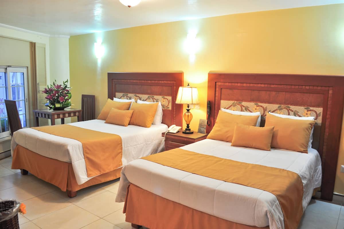 A hotel room with two beds, each with a wooden headboard, white bedding, and a yellow accent. There is a nightstand with a lamp and a telephone between the beds.