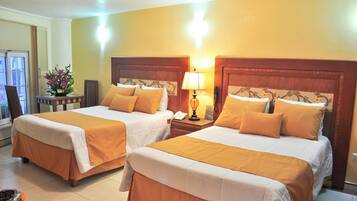 A hotel room with two beds, each with a wooden headboard, white bedding, and a yellow accent. There is a nightstand with a lamp and a telephone between the beds.