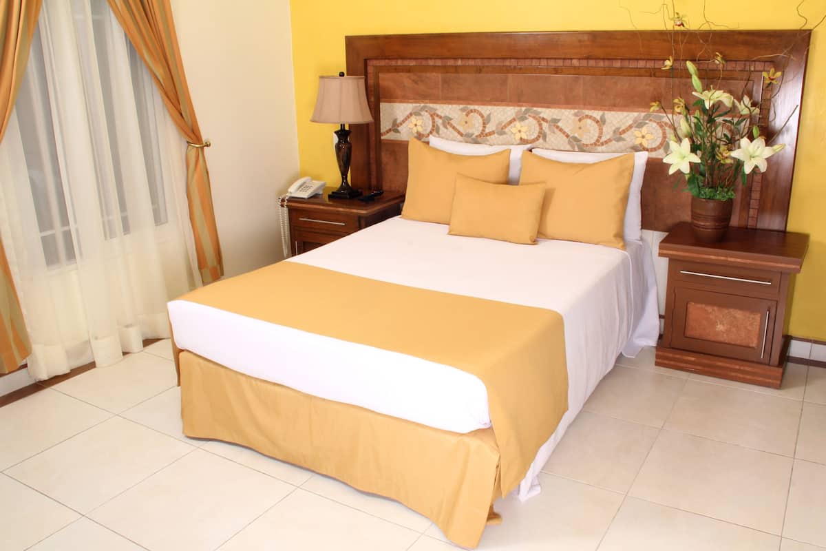 A hotel room with a large bed, a wooden headboard, a nightstand with a lamp, and a vase with flowers.