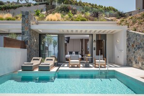 A modern outdoor pool area with lounge chairs and a stone wall backdrop. - Happy Cretan Suites (Malevizi)