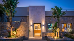 A modern building with a stone facade, a central entrance, and a restaurant visible through the windows. - Happy Cretan Suites (Malevizi)