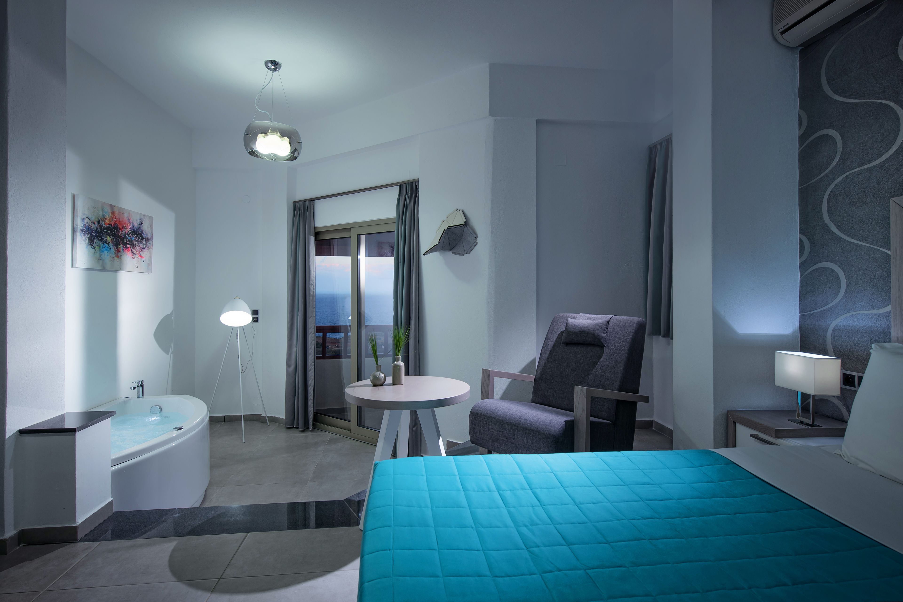 A modern hotel room with a large bed, a sitting area with a chair and table, a bathtub, and a view through a glass door.