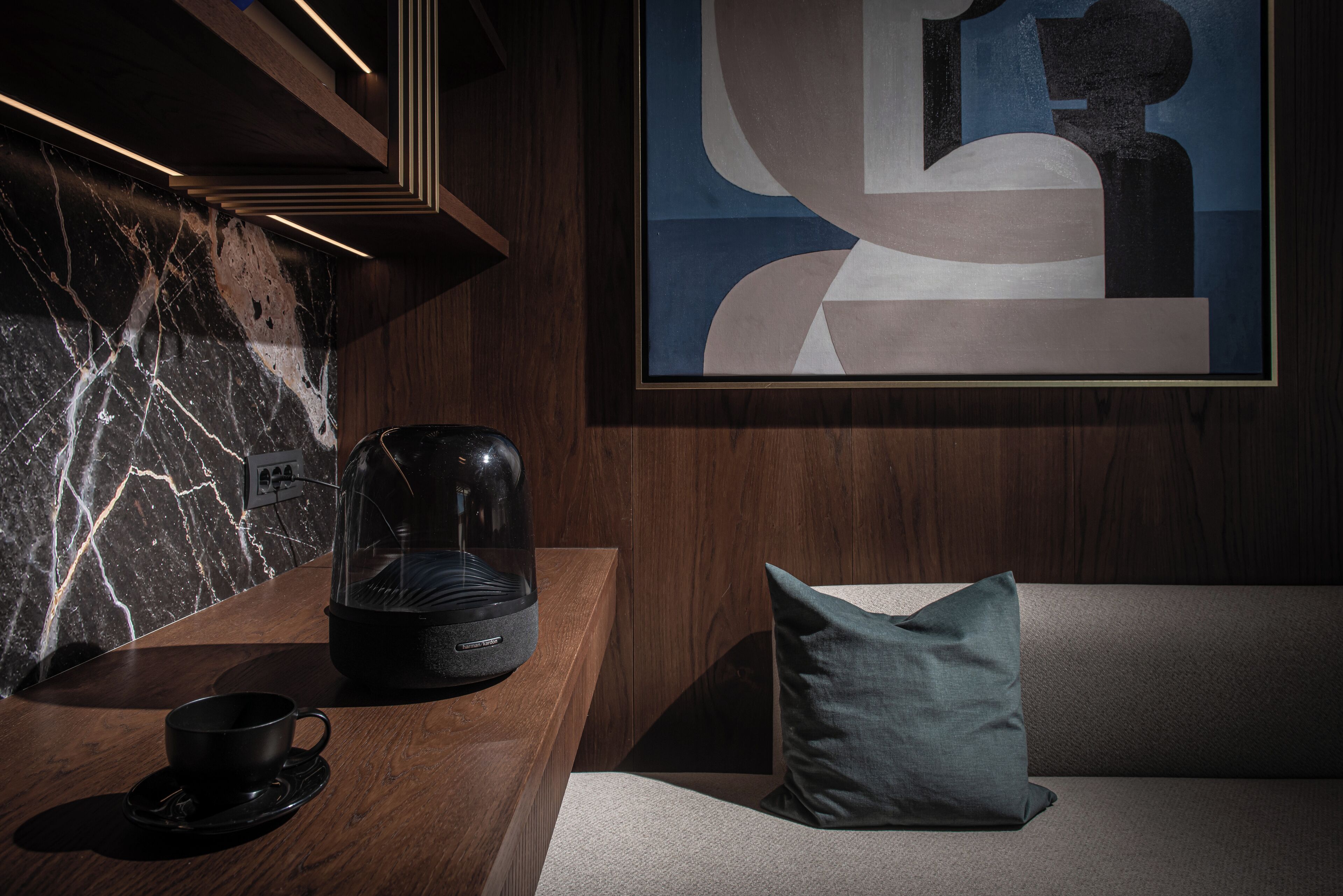A modern room with a marble wall, a coffee maker, a cup, a cushion, and a framed abstract painting.