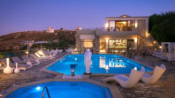 A modern pool area with lounge chairs, a hot tub, and a bar area.