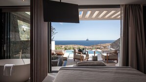 A modern bedroom with a large bed, a bathtub, and a view of the ocean. - Happy Cretan Suites (Malevizi)