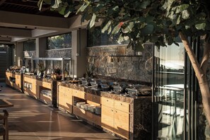 A buffet setup with a stone wall, wooden cabinets, and a glass enclosure. - Happy Cretan Suites (Malevizi)