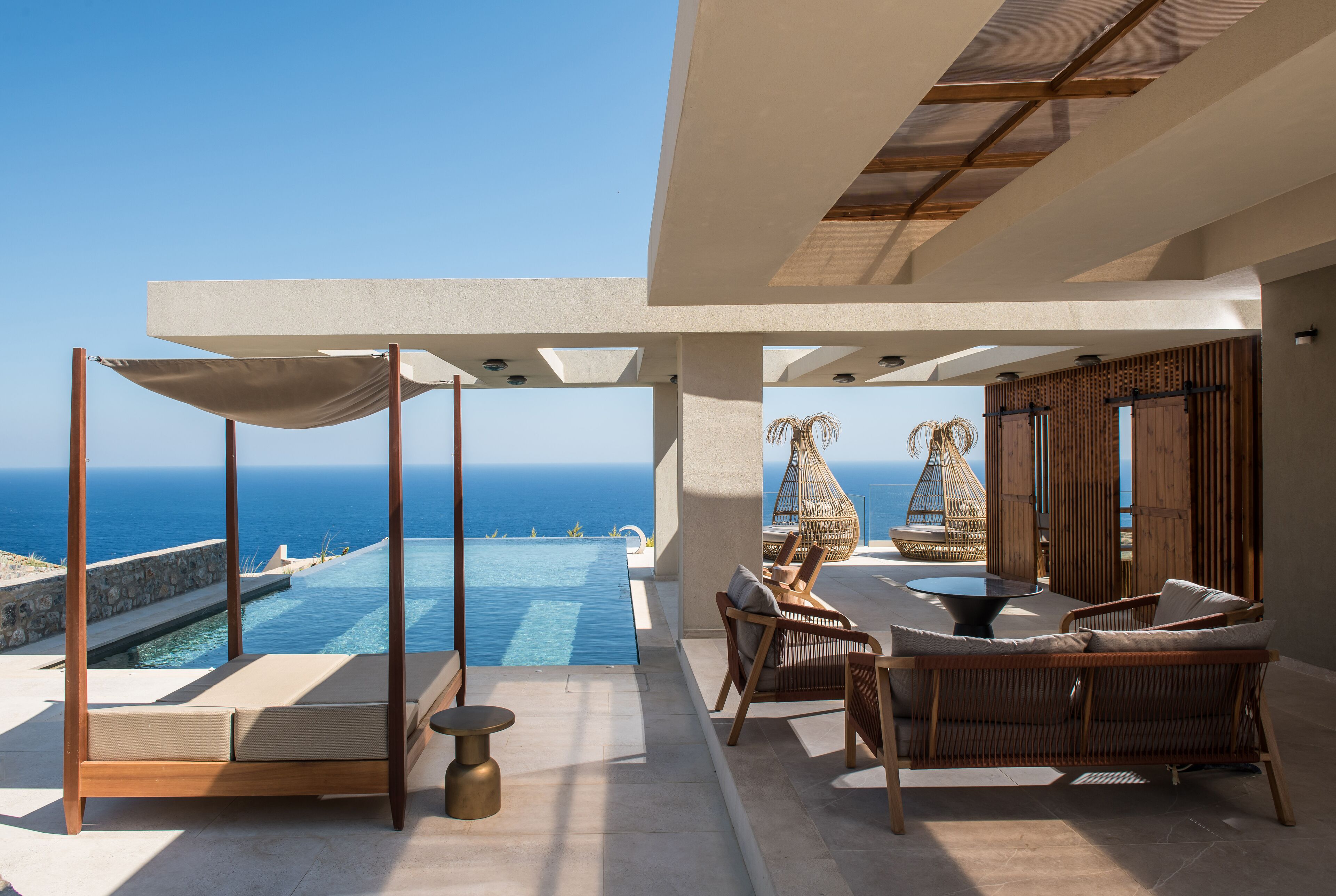 A luxurious outdoor lounge area with a pool, wicker furniture, and a view of the ocean.