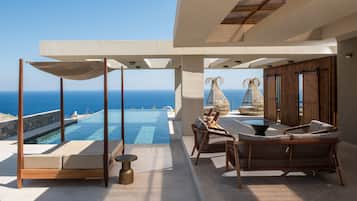 A luxurious outdoor lounge area with a pool, wicker furniture, and a view of the ocean.