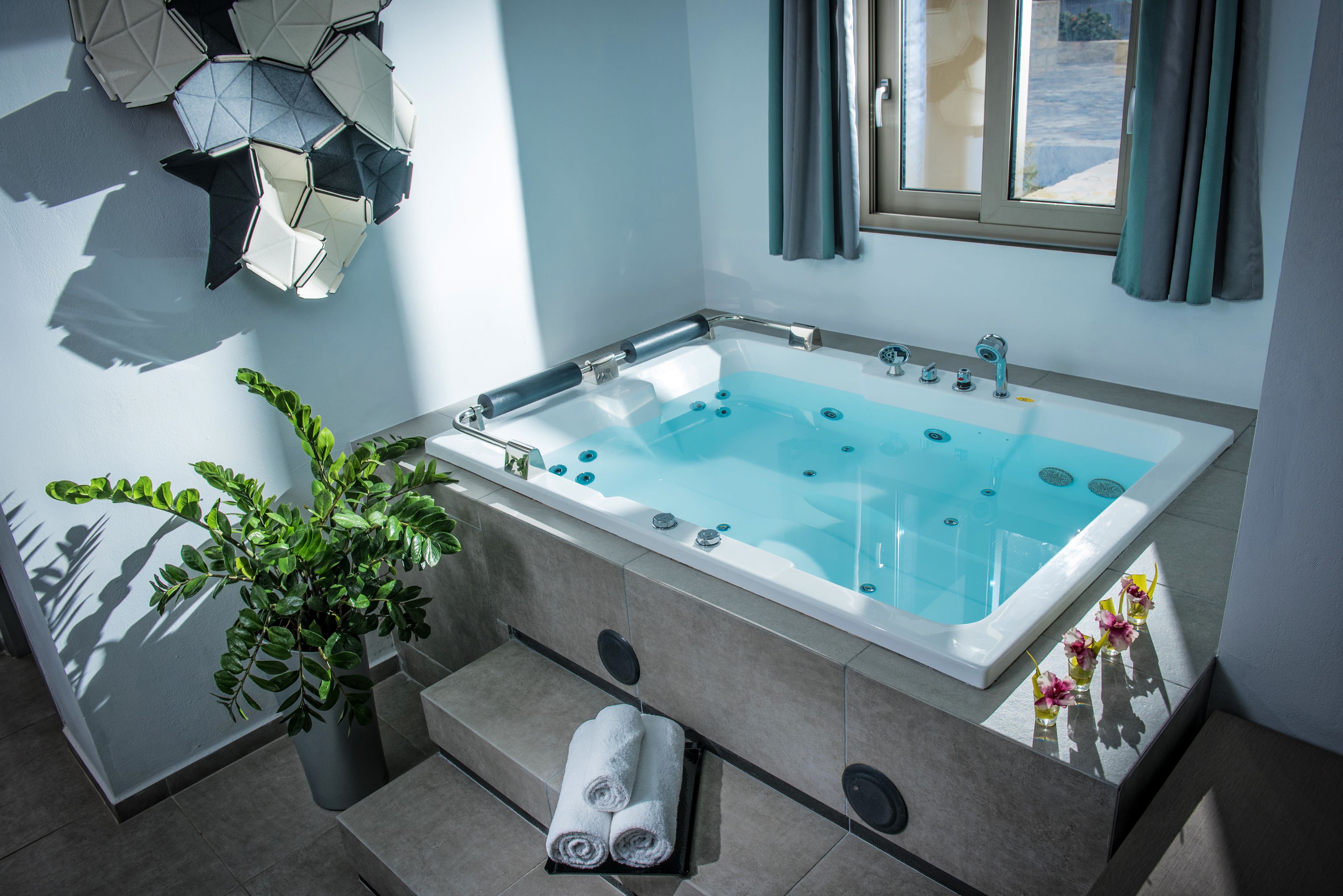 Un baño moderno con una bañera independiente, una planta en maceta y toallas ordenadamente dobladas.
