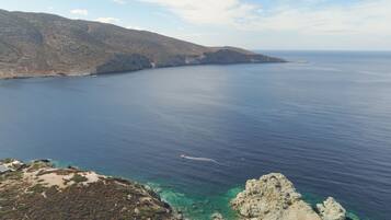 A coastal landscape with clear blue waters, rocky cliffs, and sparse vegetation.