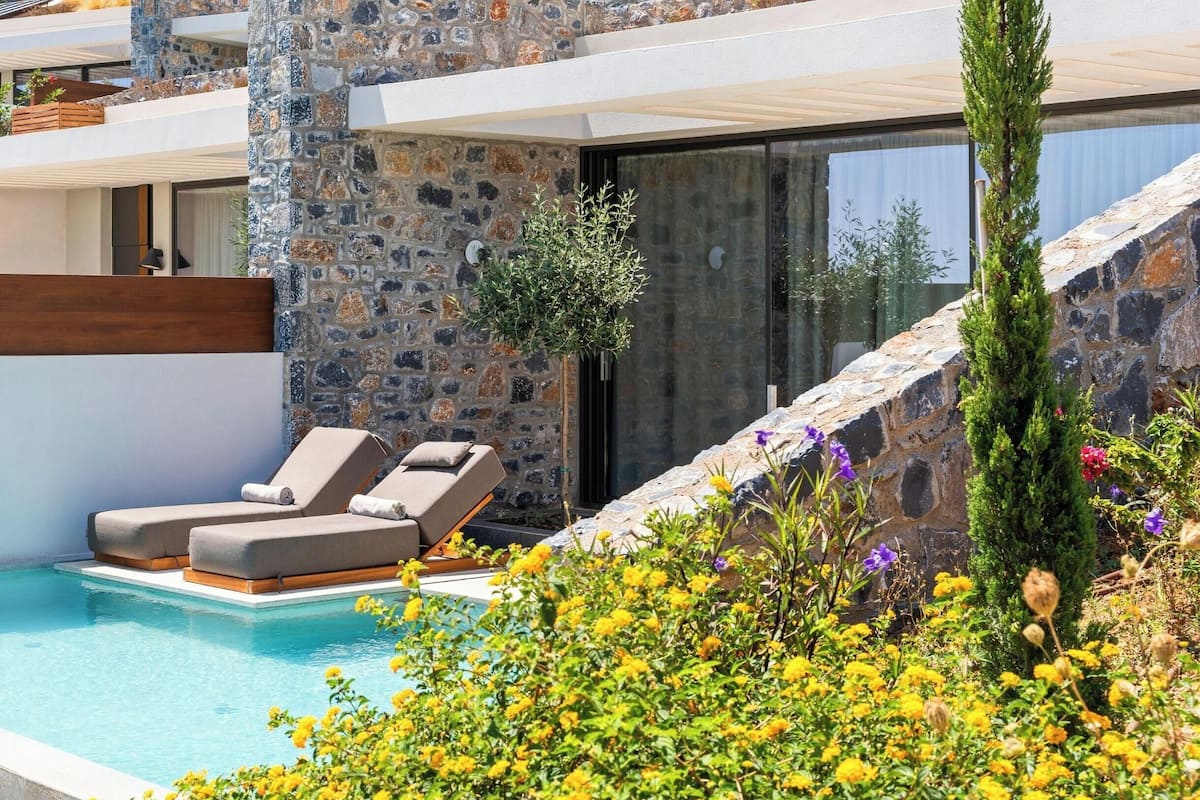 A modern pool area with lounge chairs, a stone wall, and a variety of flowers.
