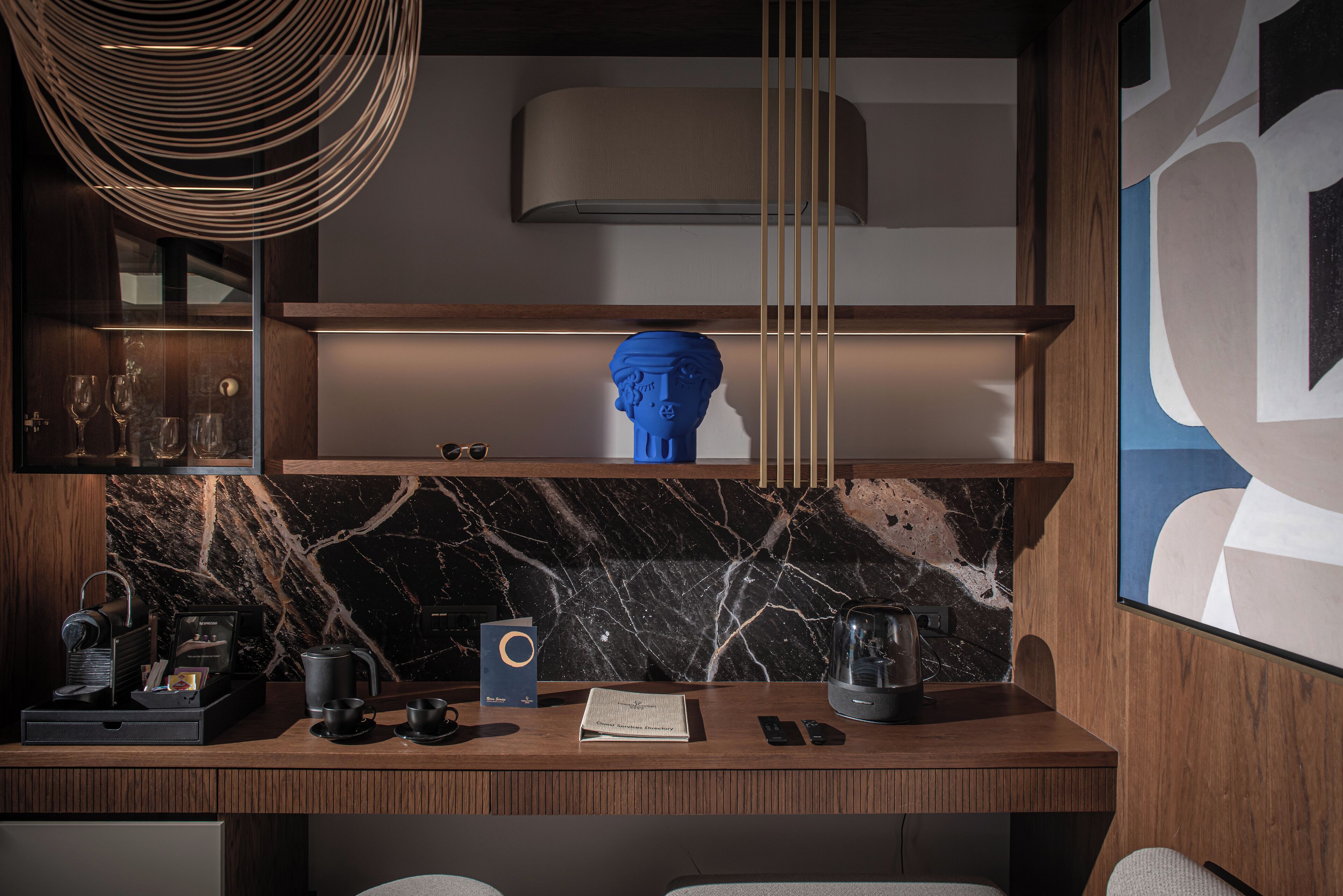 Een moderne hotelkamer met een marmeren spatwand, een houten bureau met een koffiezetapparaat, een boek en een smartphone.